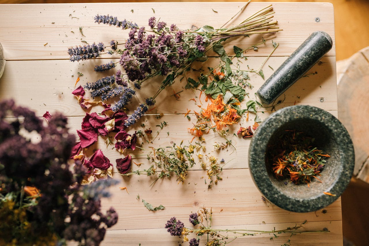 home-hero Flat lay of dried herbs and flowers with a stone mortar and pestle on a rustic wooden table.