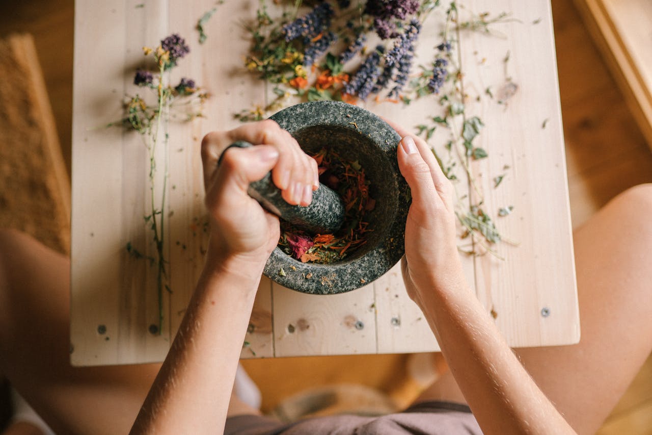 services-05 Top view of hands grinding dried herbs and petals with a mortar and pestle on a wooden table.